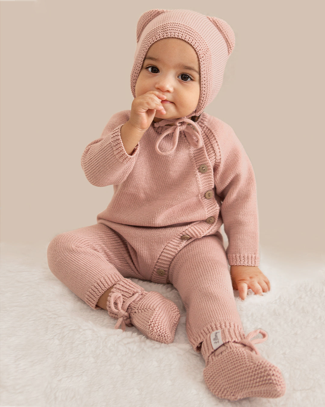 Baby in pink knitted outfit with matching hat on a light background