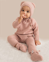 Baby in pink knitted outfit with matching hat on a light background
