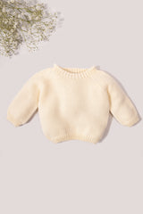 Cream-colored baby sweater on a light gray background with a small bouquet of flowers.