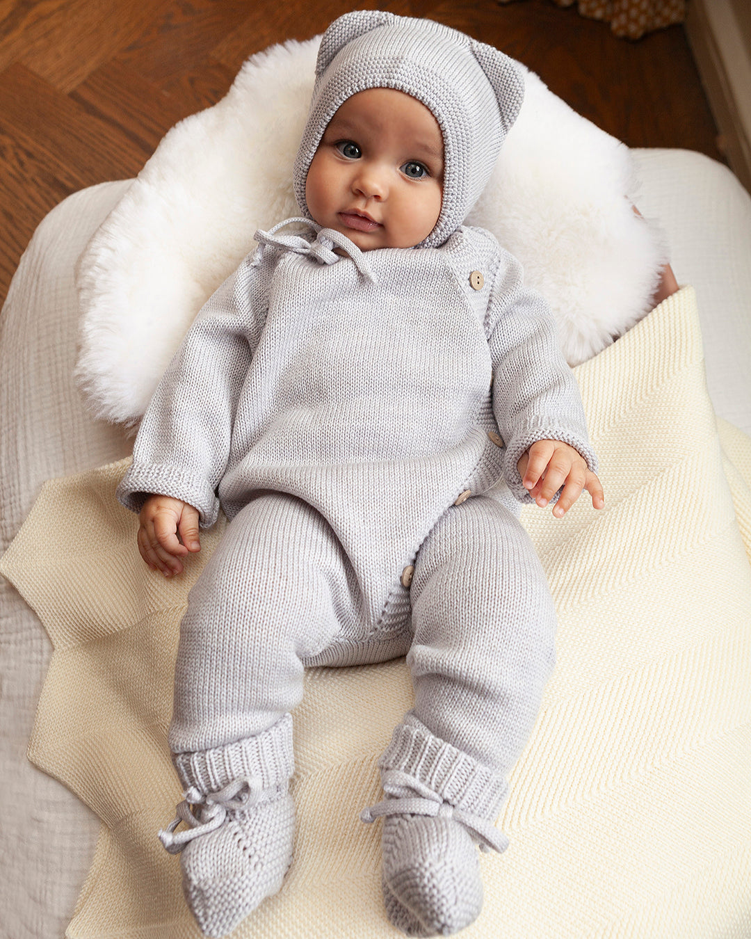 Baby in a gray knit outfit sitting on a soft surface