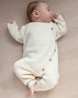 Baby wearing a white knitted outfit lying on a textured surface
