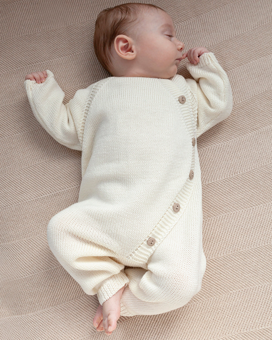 Baby wearing a white knitted outfit lying on a textured surface